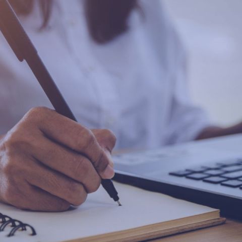 A man in a denim jacket sits at a table, focused on their laptop, with various office elements in th